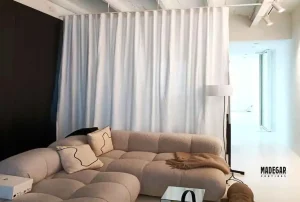 Cortina separadora de ambientes confeccionada en loneta de algodón blanca instalada con el sistema de onda perfecta de Madegar Cortinas, suspendida en medio de un salón comedor diáfano en un loft moderno de Barcelona.