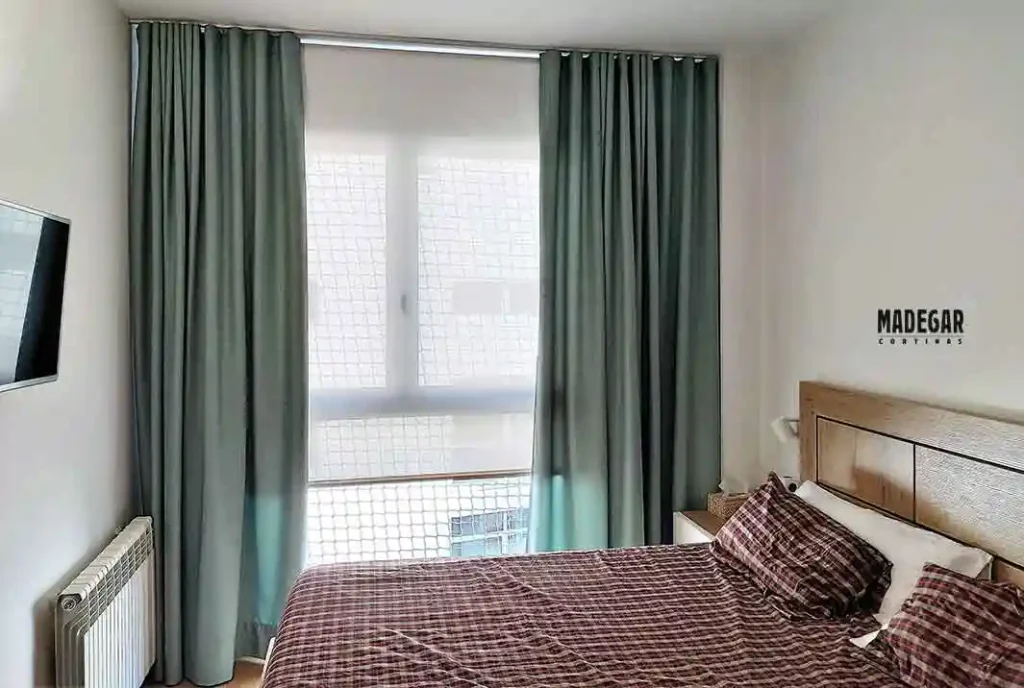 Dormitorio moderno con estor enrollable screen a medida al 1% de apertura combinado con dobles cortinas tradicionales de caída informal en color verde a ambos lados del ventanal.