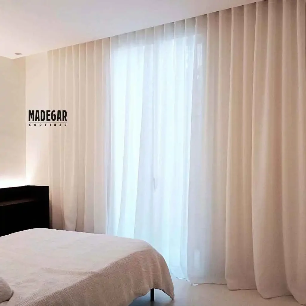 Cortina convencional a medida de Cortinas Madegar confeccionada en lino 100% natural de color crudo, instalada a onda perfecta y arrastrando sutilmente sobre el suelo de microcemento de un dormitorio principal en un loft del Eixample, filtrando la luz exterior con elegancia y sofisticación.