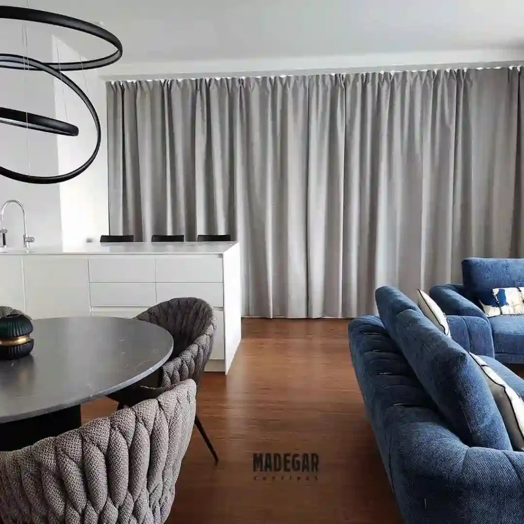 Cortinas convencionales blackout de caída gris con textura textil premium instaladas de techo a suelo en un salón con cocina abierta de alto standing en Diagonal Mar.