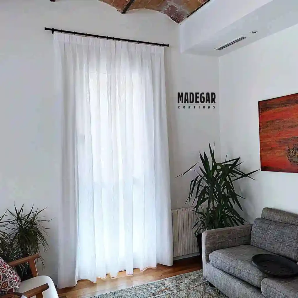 Cortinas convencionales blancas a tablas con un riel decorativo negro de estilo industrial que remata un salón con techo de volta catalana en Gràcia.