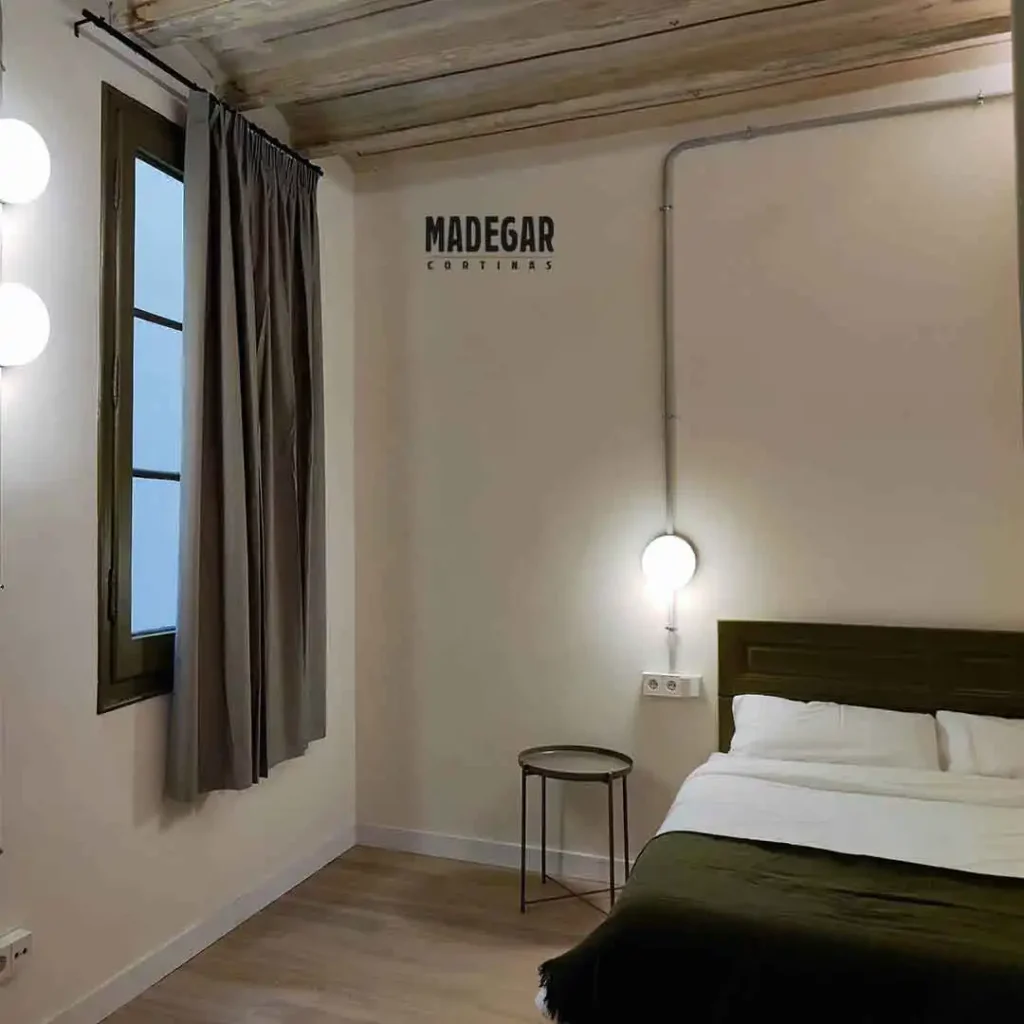 Cortinas convencionales acústicas de color gris en un dormitorio de matrimonio sencillo con cabecero verde y techo tradicional de vigas en un piso de la Barceloneta.