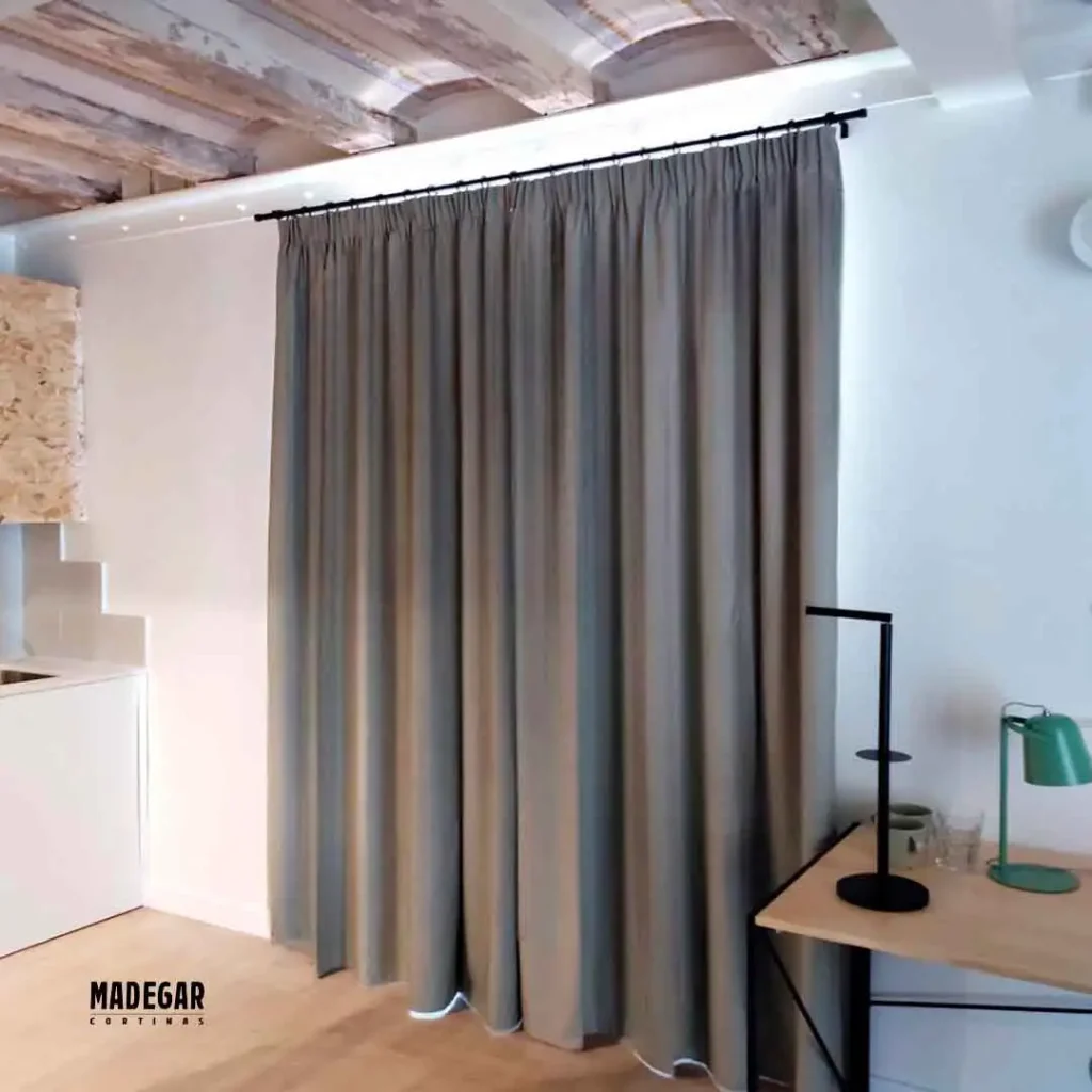 Cortinas acústicas a medida en tono gris arena colgadas de rieles negros en un despacho con mesa de madera y lámparas de diseño industrial en la Barceloneta.