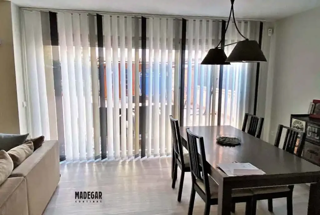 Cortinas verticales de lamas screen a medida en tonos blanco y gris oscuro de Madegar, regulando el sol en el gran ventanal de un comedor de diseño moderno en Sarrià-Sant Gervasi, Barcelona