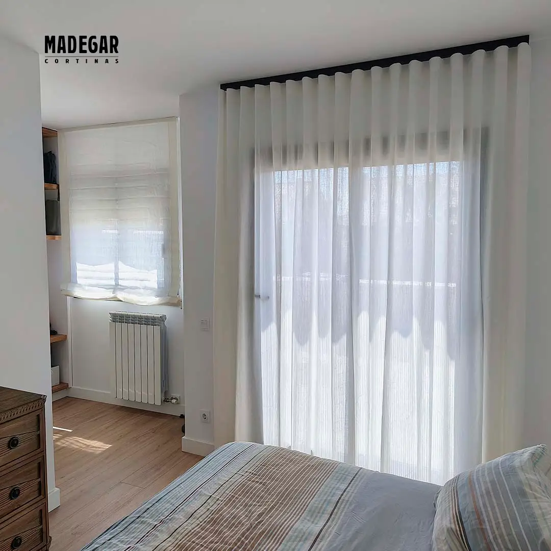 Cortinas de lino blanco a juego con un estor paqueto en otra ventana de un dormitorio en una casa unifamiliar de Teià