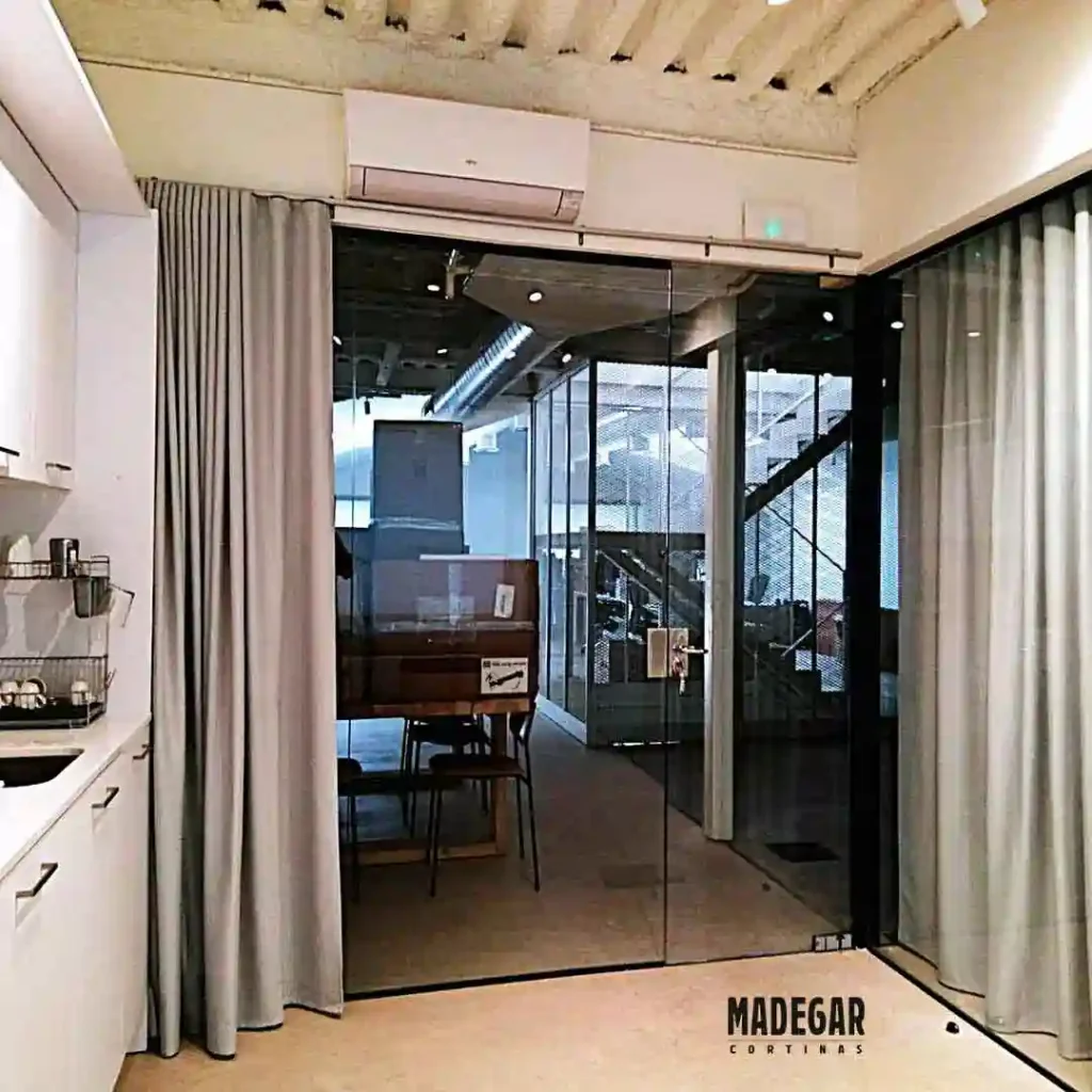 Cortinas acústicas separadoras de ambientes en posición abierta dentro de una oficina moderna en el 22@ de Barcelona. La instalación a medida de Madegar Cortinas permite integrar o independizar espacios de trabajo de forma dinámica.