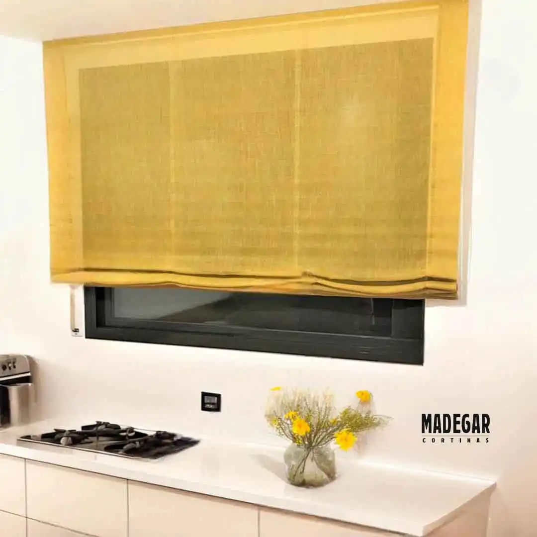 Solución decorativa para ventanas de cocina en Poblenou: estor de lino amarillo texturizado confeccionado a medida por Madegar Cortinas. La tela de lino aporta un toque de calidez y alegría instantánea a un espacio minimalista blanco. Se muestra cómo el estor a medida encaja perfectamente sobre la ventana negra horizontal de la cocina moderna.