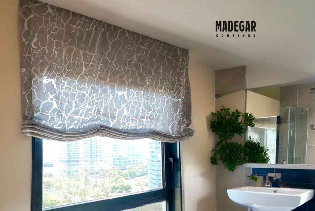 Estor paqueto a medida con tejido devoré instalado en un baño de alto standing en Diagonal Mar, Barcelona. La tela juega con las transparencias en el patrón mientras el fondo más tupido asegura la privacidad, todo confeccionado por Madegar Cortinas.