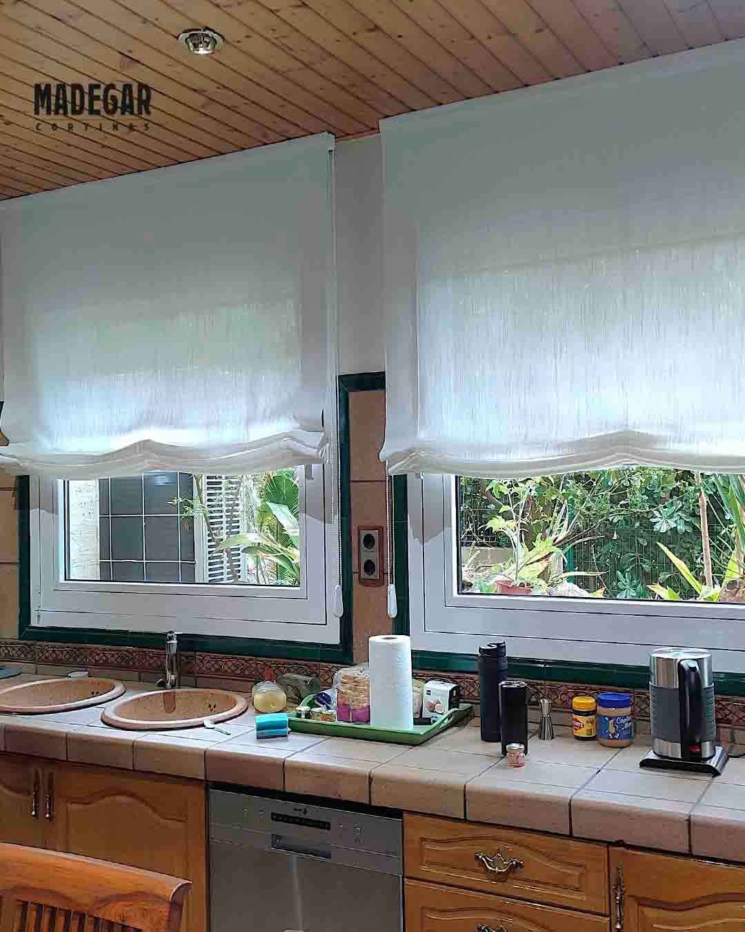 Detalle de estores paquetos confeccionados en semi lino color natural para la ventana de una cocina en La Garriga, Barcelona. La tela tamiza la luz de forma suave sobre la encimera, creando un ambiente cálido y muy hogareño.