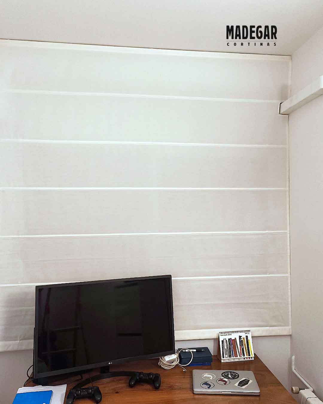 Estor de loneta blanco con varillas instalado en un despacho del Eixample, Barcelona, por Madegar Cortinas. Se aprecia el recorte a medida en la esquina inferior derecha para que el estor baje perfecto alrededor de la canaleta del aire acondicionado sin estorbar. El estor cubre el ventanal sobre un escritorio