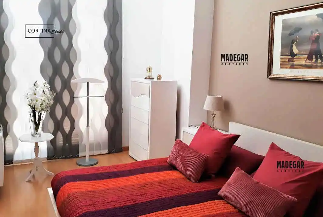 Dormitorio de lujo en Sant Cugat decorado con cortinas verticales bicolor de lamas onduladas. El diseño vanguardista en blanco y gris de Madegar Cortinas crea un juego de sombras dinámico que complementa la decoración moderna y textil de la habitación.