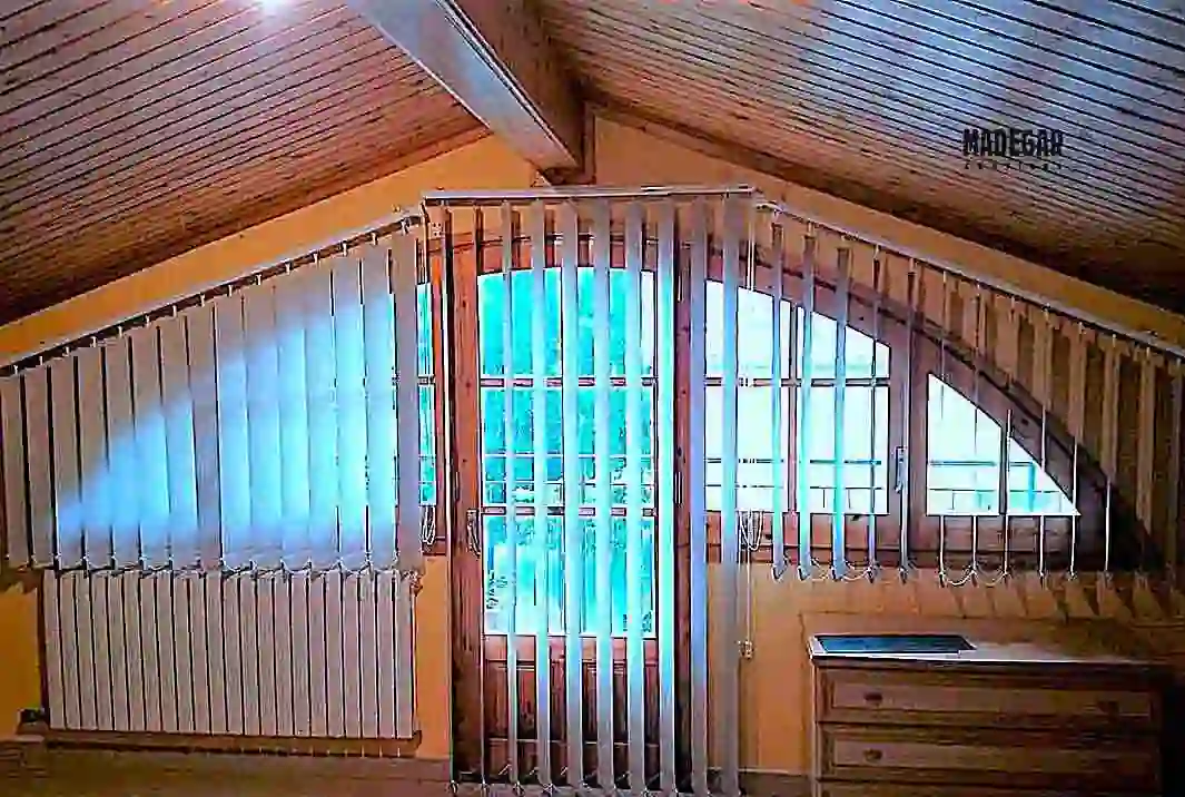 Instalación de cortinas verticales con tejido blackout en una buhardilla de Sant Cugat. Las lamas de Madegar Cortinas tamizan la entrada de luz y mejoran el aislamiento térmico en techos inclinados con vigas de madera.
