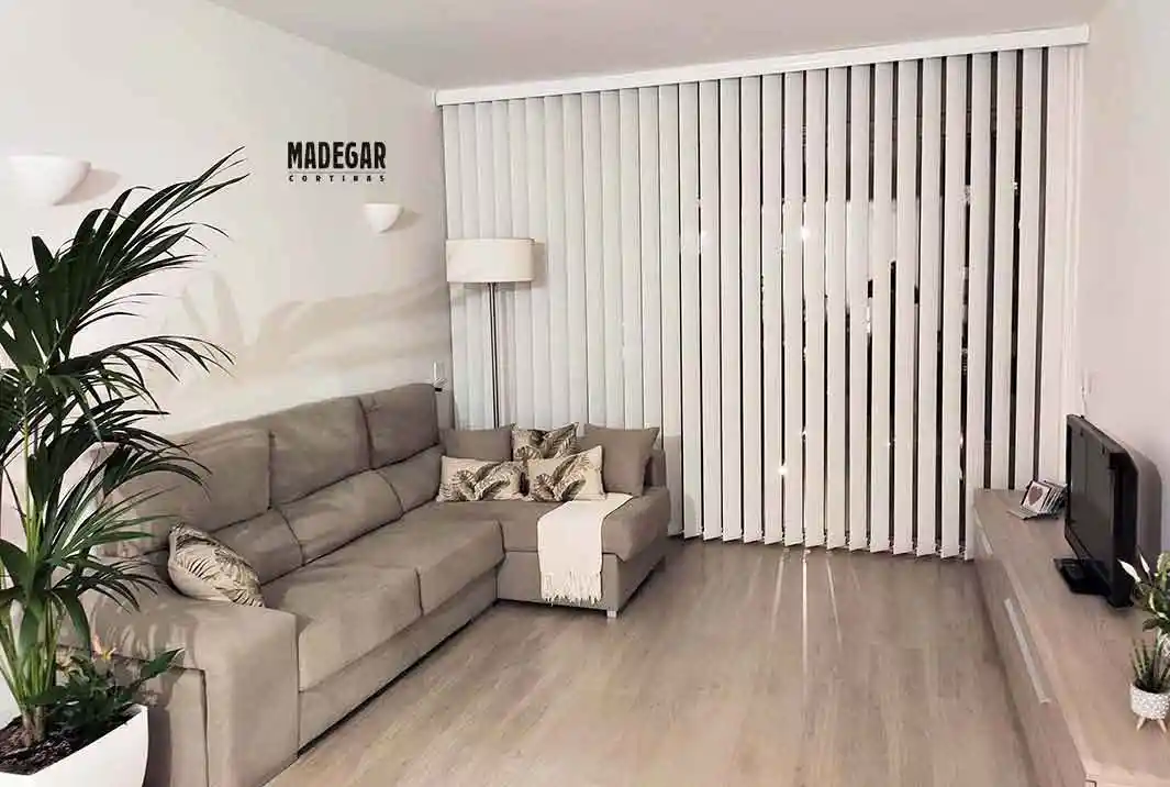 Detalle de cortina vertical a medida en tejido screen blanco cubriendo el ventanal de un salón moderno en Sarrià-Sant Gervasi, Barcelona. Las lamas están parcialmente giradas para controlar la entrada de luz y la privacidad, instaladas por Madegar Cortinas.
